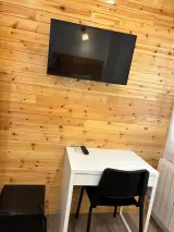 Televisor de pantalla plana en pared de madera sobre un escritorio blanco con silla y minibar